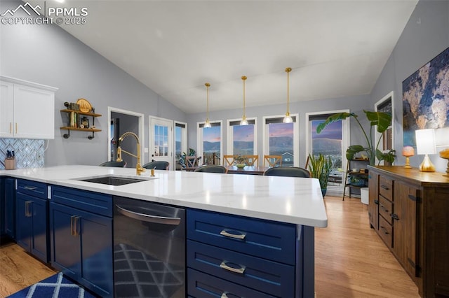 kitchen with stainless steel dishwasher, a sink, blue cabinetry, light countertops, and light wood-style flooring