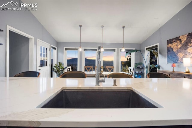 kitchen with lofted ceiling, a sink, light stone counters, open floor plan, and hanging light fixtures