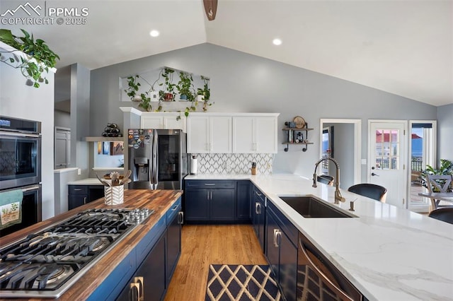 kitchen with a sink, appliances with stainless steel finishes, lofted ceiling, white cabinetry, and blue cabinets