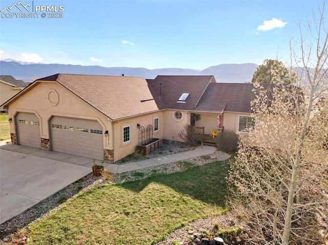 view of front of home featuring an attached garage, stucco siding, a mountain view, and a front lawn