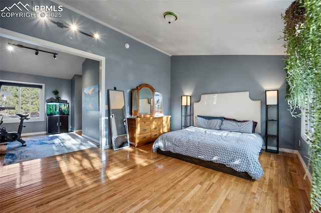 bedroom with hardwood / wood-style floors, track lighting, and baseboards