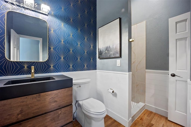full bathroom featuring a wainscoted wall, toilet, wood finished floors, vanity, and wallpapered walls