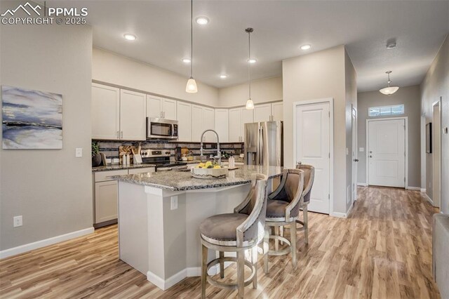1341 Solitaire St, Colorado Springs, CO 80905 - kitchen featuring a sink, light stone counters, light wood-style flooring, a kitchen island with sink, and appliances with stainless steel finishes