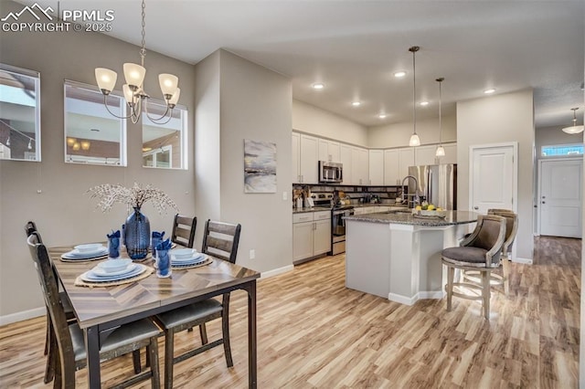 1341 Solitaire St, Colorado Springs, CO 80905 - kitchen featuring white cabinets, light wood finished floors, appliances with stainless steel finishes, an island with sink, and an inviting chandelier