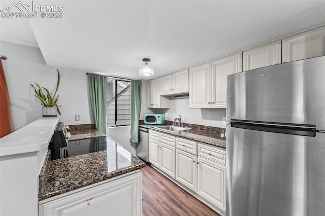 kitchen with appliances with stainless steel finishes, a sink, white cabinetry, and dark stone countertops