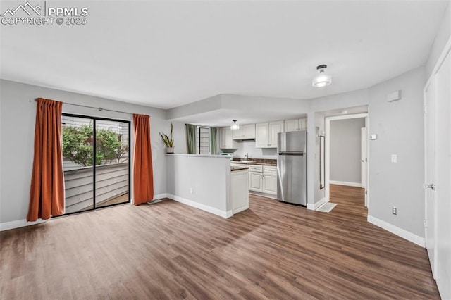 kitchen with freestanding refrigerator, a peninsula, baseboards, and wood finished floors