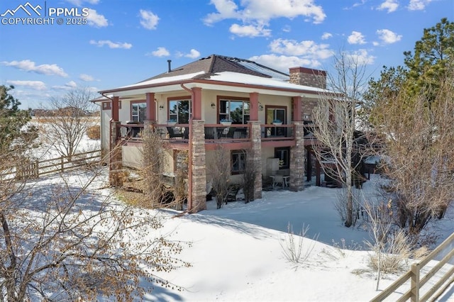 snow covered back of property with stucco siding and a chimney