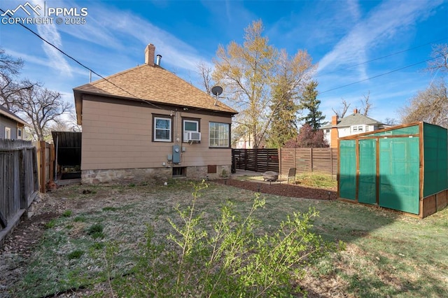 back of property with an outbuilding, an exterior structure, a fenced backyard, and roof with shingles
