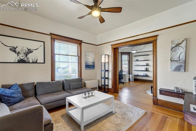 living area with baseboards, light wood-type flooring, and a ceiling fan
