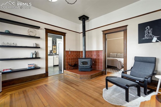sitting room featuring a wood stove, tile walls, a wainscoted wall, and wood finished floors