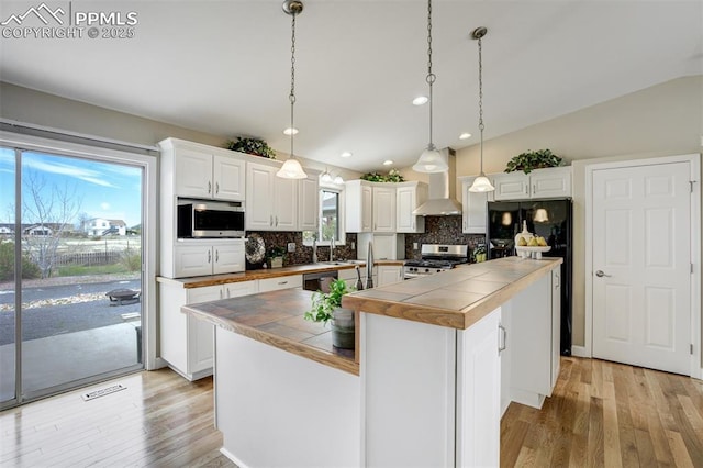 kitchen with tile counters, wall chimney range hood, appliances with stainless steel finishes, and decorative backsplash