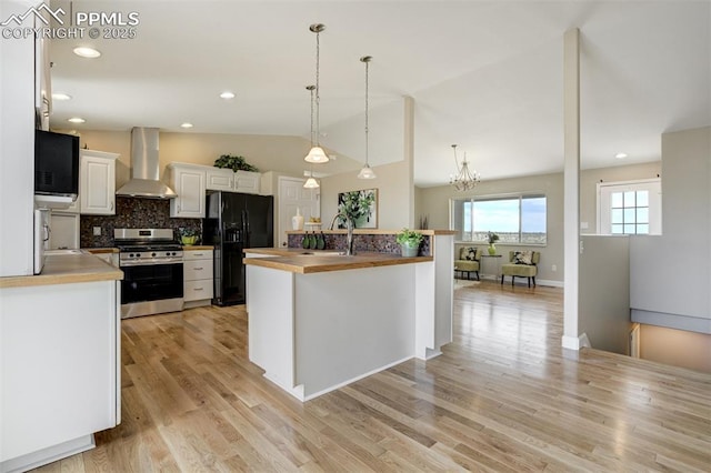 kitchen with wall chimney range hood, stainless steel range with gas cooktop, tasteful backsplash, white cabinetry, and black fridge