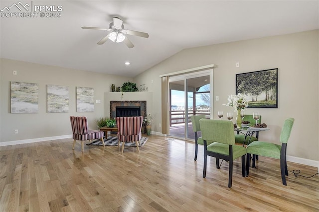 living area featuring vaulted ceiling, a ceiling fan, light wood-type flooring, a fireplace, and baseboards