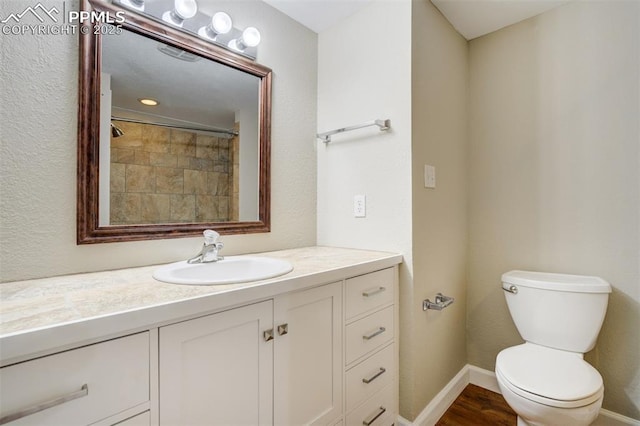 bathroom with wood finished floors, toilet, vanity, baseboards, and walk in shower