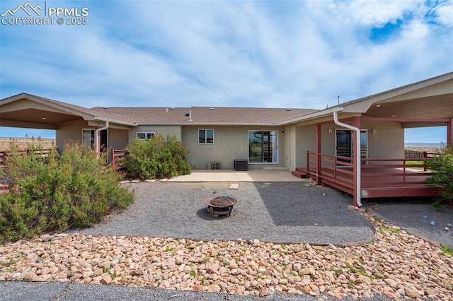 rear view of house with stucco siding, a deck, a patio, and an outdoor fire pit
