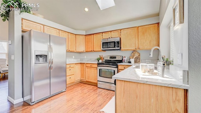 kitchen featuring light brown cabinets, a skylight, light wood-style floors, stainless steel appliances, and light stone countertops