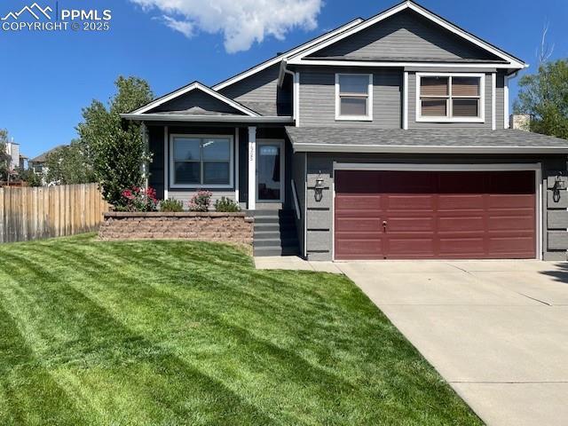 tri-level home featuring an attached garage, a front lawn, fence, and concrete driveway