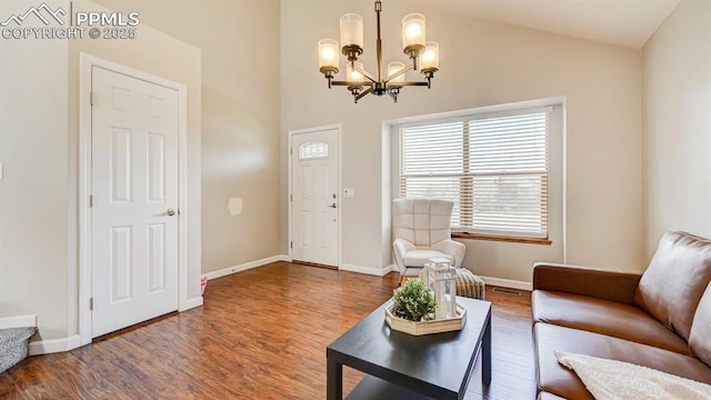 living room featuring lofted ceiling, wood finished floors, baseboards, and a notable chandelier