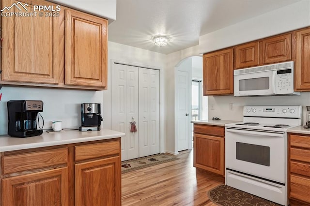 13255 Woodlake Rd, Elbert, CO 80106 - kitchen with white appliances, brown cabinets, light wood-style flooring, arched walkways, and light countertops
