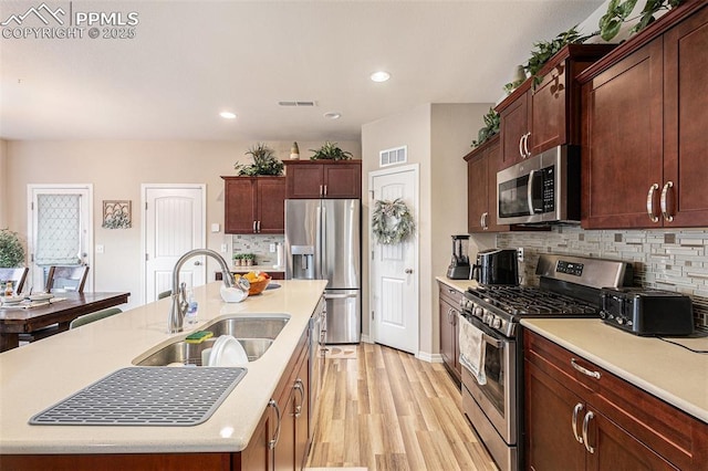 kitchen with a sink, stainless steel appliances, light wood-style floors, a center island with sink, and visible vents