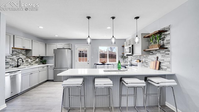 kitchen featuring light countertops, a sink, open shelves, appliances with stainless steel finishes, and a peninsula