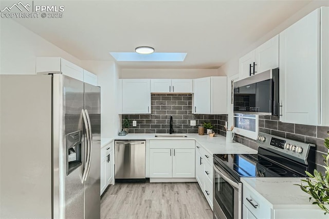 kitchen with a sink, light wood finished floors, white cabinetry, a skylight, and appliances with stainless steel finishes