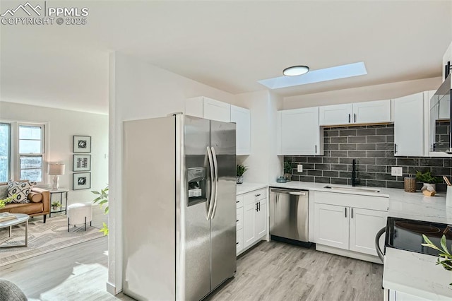 kitchen featuring light countertops, a skylight, appliances with stainless steel finishes, a sink, and backsplash