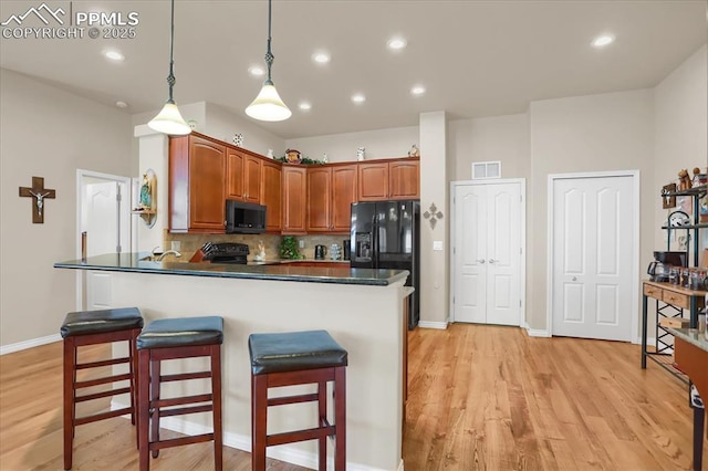 kitchen with decorative backsplash, visible vents, a breakfast bar, dark countertops, and black appliances