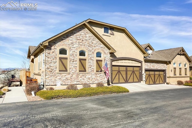 view of front facade featuring driveway, stucco siding, an attached garage, and stone siding