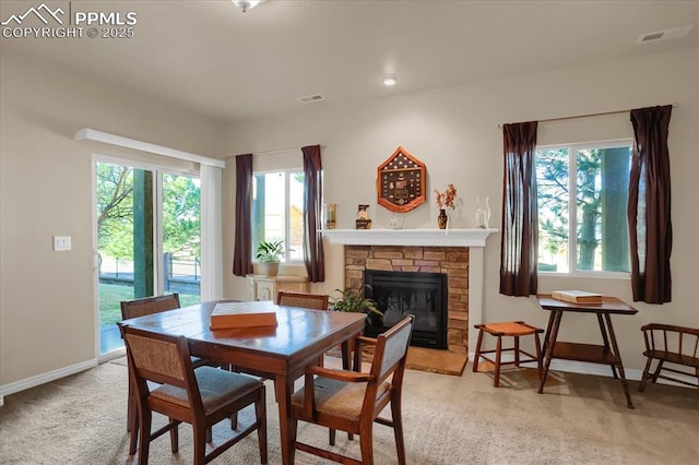 dining room featuring a stone fireplace, baseboards, and light carpet