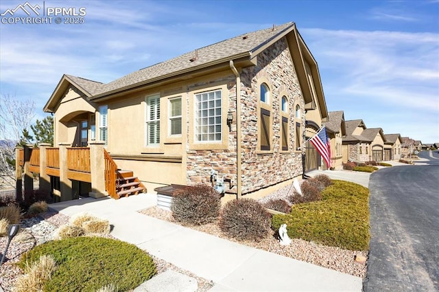 view of side of home featuring stone siding, driveway, stucco siding, and a deck