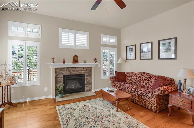 living room with wood finished floors, a stone fireplace, baseboards, and ceiling fan