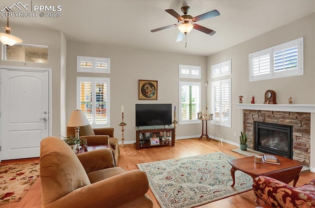 living area with baseboards, ceiling fan, wood finished floors, and a stone fireplace