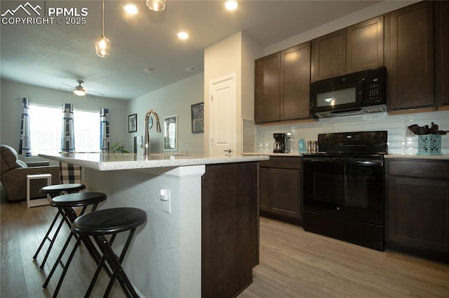 kitchen with light wood-style flooring, a ceiling fan, open floor plan, a breakfast bar area, and black appliances