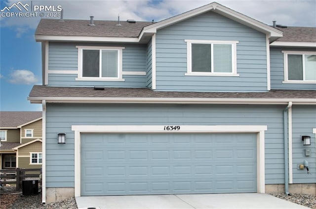 view of front facade featuring a shingled roof, cooling unit, an attached garage, and concrete driveway