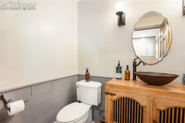 half bathroom featuring vanity, wainscoting, and toilet