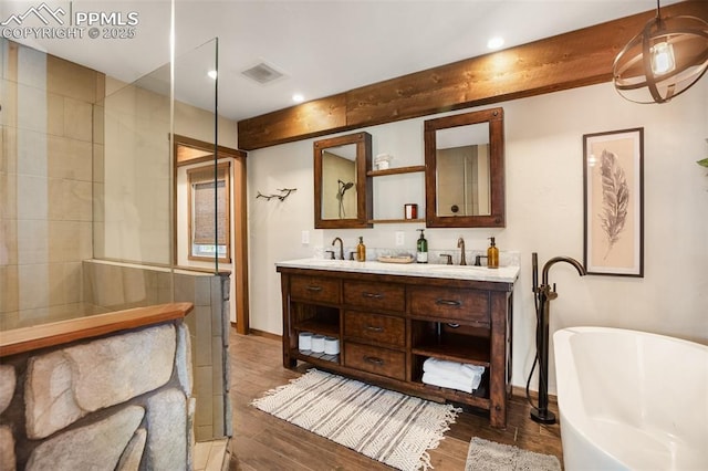 full bath featuring double vanity, visible vents, a freestanding bath, wood finished floors, and a sink