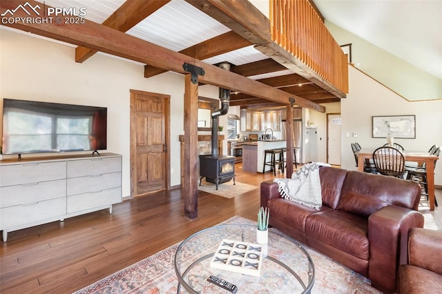 living room with beamed ceiling, wood finished floors, and a wood stove