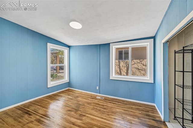 empty room featuring lofted ceiling, wood finished floors, visible vents, and baseboards