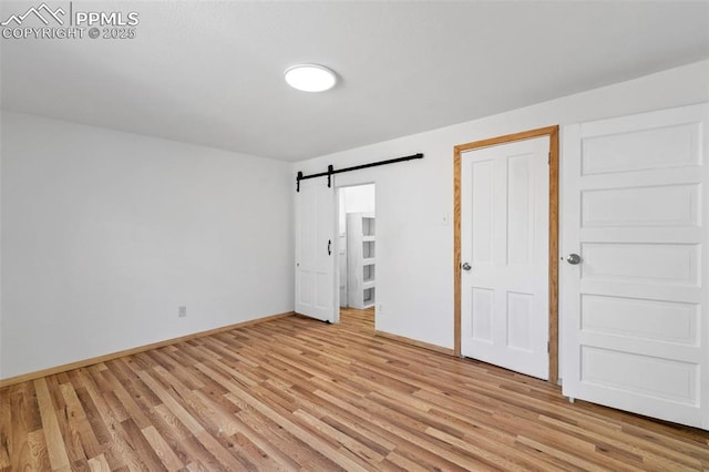 unfurnished bedroom featuring light wood-style flooring, baseboards, and a barn door