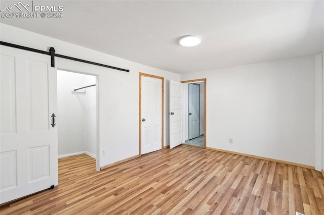 unfurnished bedroom with a barn door, light wood finished floors, and baseboards