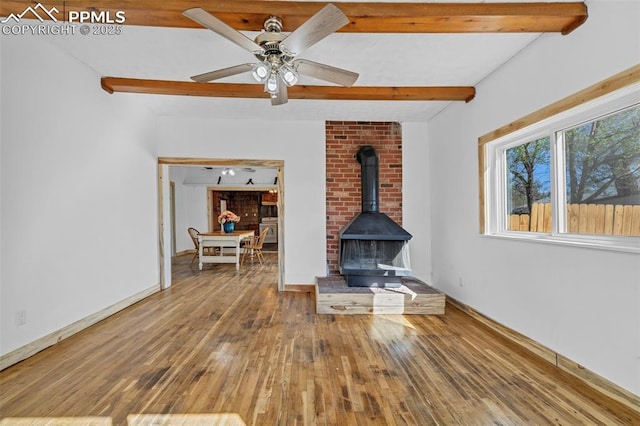 unfurnished living room with wood-type flooring, beam ceiling, a wood stove, and a ceiling fan