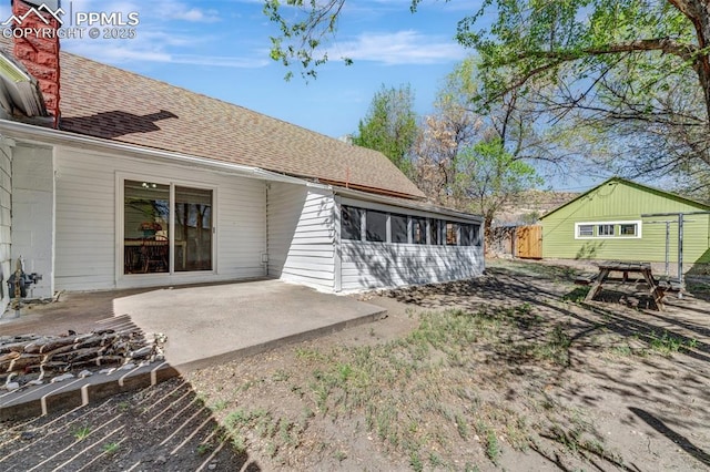 rear view of house featuring a sunroom, fence, a patio, and a shingled roof