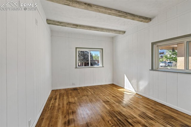 spare room featuring beamed ceiling, hardwood / wood-style floors, a healthy amount of sunlight, and visible vents