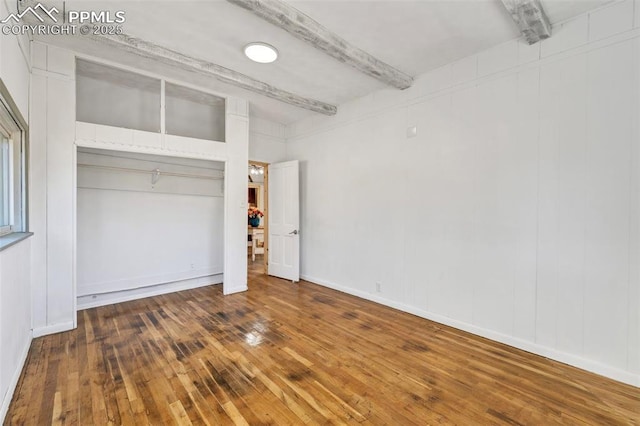 unfurnished bedroom featuring beam ceiling, a closet, and wood-type flooring