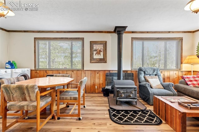 interior space featuring wainscoting, a wood stove, a textured ceiling, wood walls, and light wood-type flooring