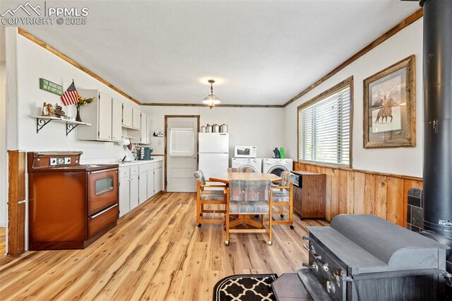 dining area featuring independent washer and dryer, wainscoting, a wood stove, light wood finished floors, and ornamental molding
