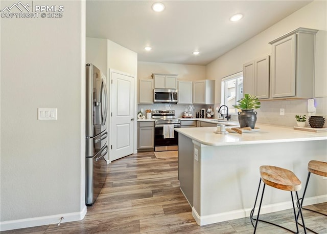 kitchen with backsplash, a sink, a peninsula, light wood-style flooring, and stainless steel appliances