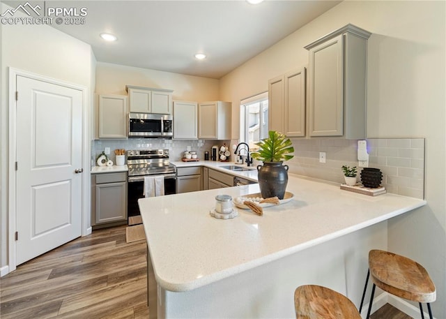kitchen with a sink, wood finished floors, appliances with stainless steel finishes, a peninsula, and gray cabinetry