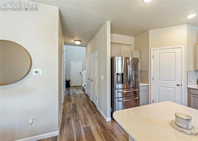 kitchen featuring backsplash, light stone countertops, stainless steel fridge, baseboards, and dark wood-style flooring